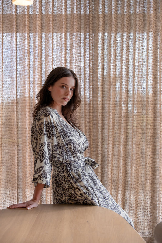 Woman in a patterned dress standing against a textured beige wall.