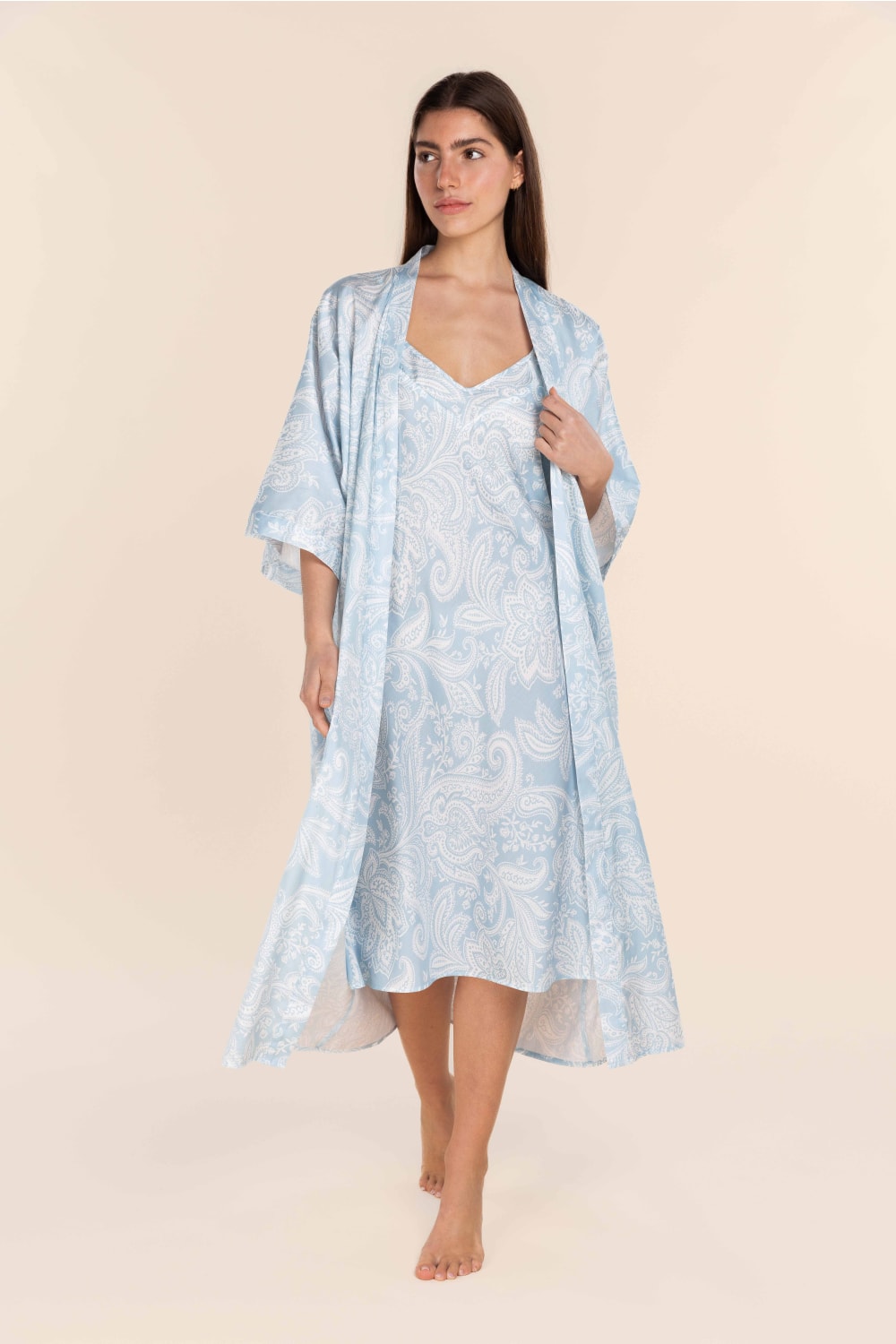 Woman wearing a light blue floral dress with a matching kimono-style cover-up on a beige background