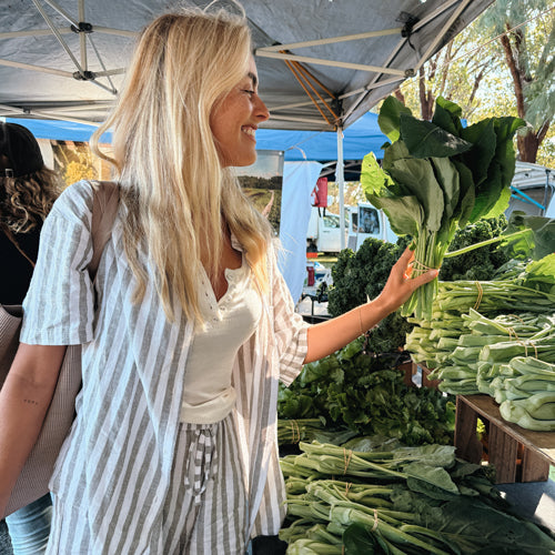 Woman shopping at a farmers market with green vegetables