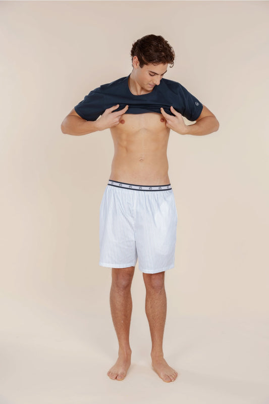 Man wearing white boxer shorts with a blue and white striped waistband on a beige background