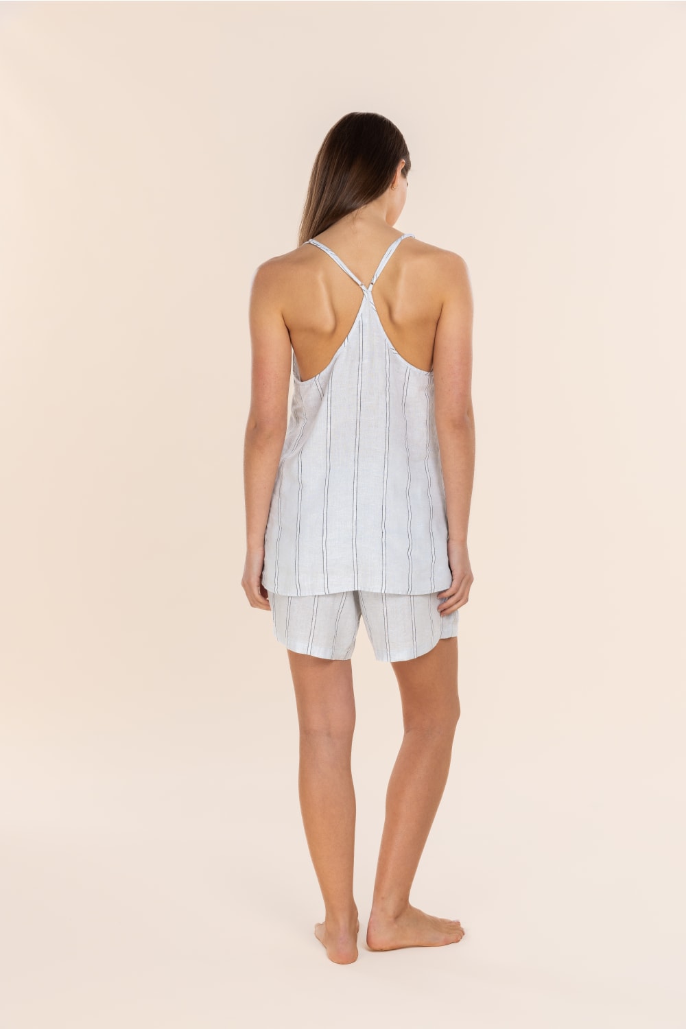 Woman wearing a light blue striped tank top and white shorts on a beige background
