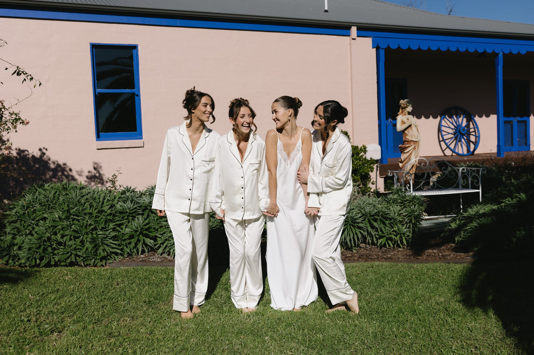Bride in an ivory satin slip nightgown walking with three bridesmaids in matching ivory satin pyjama sets on the wedding morning