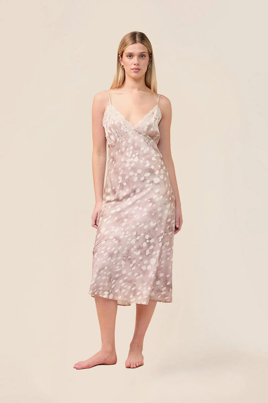 A woman modeling a light pink slip dress with a white floral pattern, standing against a solid beige background.