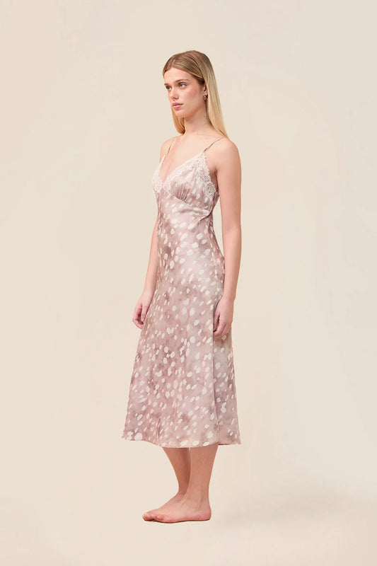 A woman modeling a sleeveless midi slip dress with thin straps and an allover small floral print in blush pink and white, standing against a plain beige studio background.