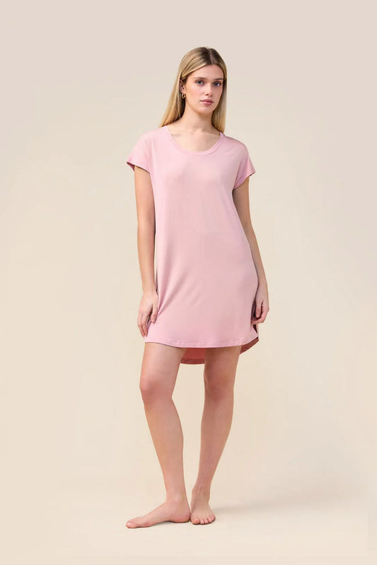 A woman modeling a light pink short-sleeve nightgown or tunic dress against a plain beige studio background.