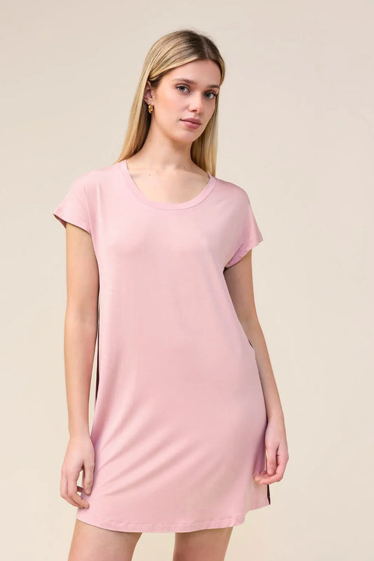 A woman modeling a light pink short-sleeve t-shirt dress against a plain beige studio background.