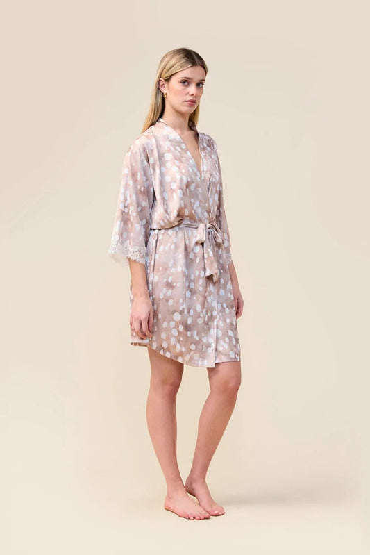 A woman modeling a short wrap robe with a beige and white floral pattern, standing against a solid beige studio background.