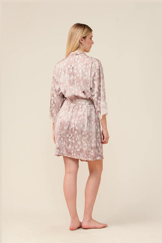 A woman stands barefoot against a plain beige studio background, shown from the back wearing a light pink robe with a white floral pattern.
