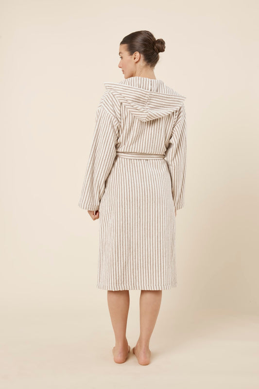 Back view of woman wearing a striped adriana terry towel robe in biscuit colour standing against a plain background