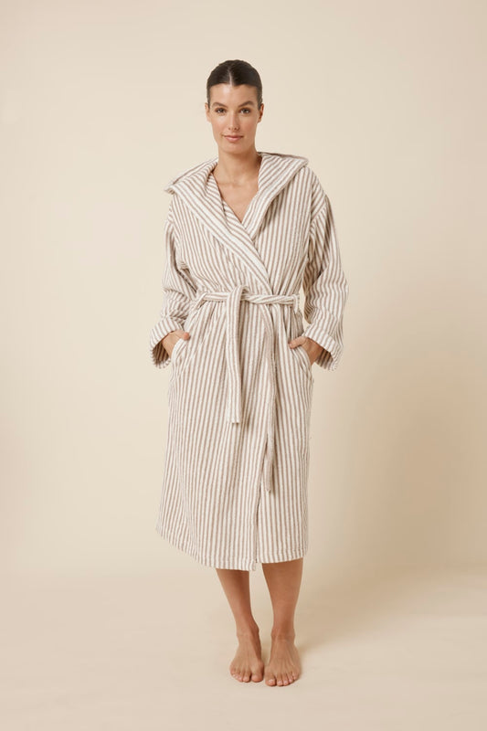Woman wearing a striped adriana terry towel robe in biscuit colour standing against a plain background