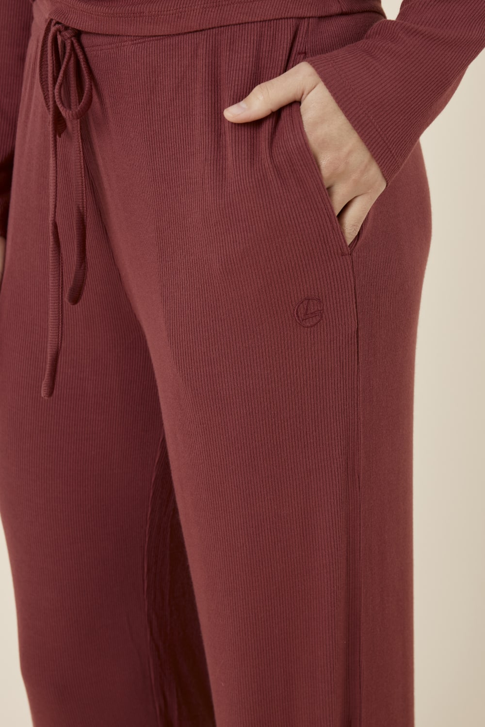 Burgundy Athens ribbed Long pant detail shot with drawstring and embroidery detail while woman has hand in her pocket
