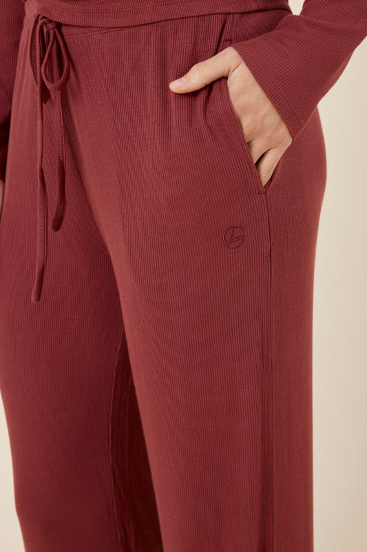 Burgundy Athens ribbed Long pant detail shot with drawstring and embroidery detail while woman has hand in her pocket