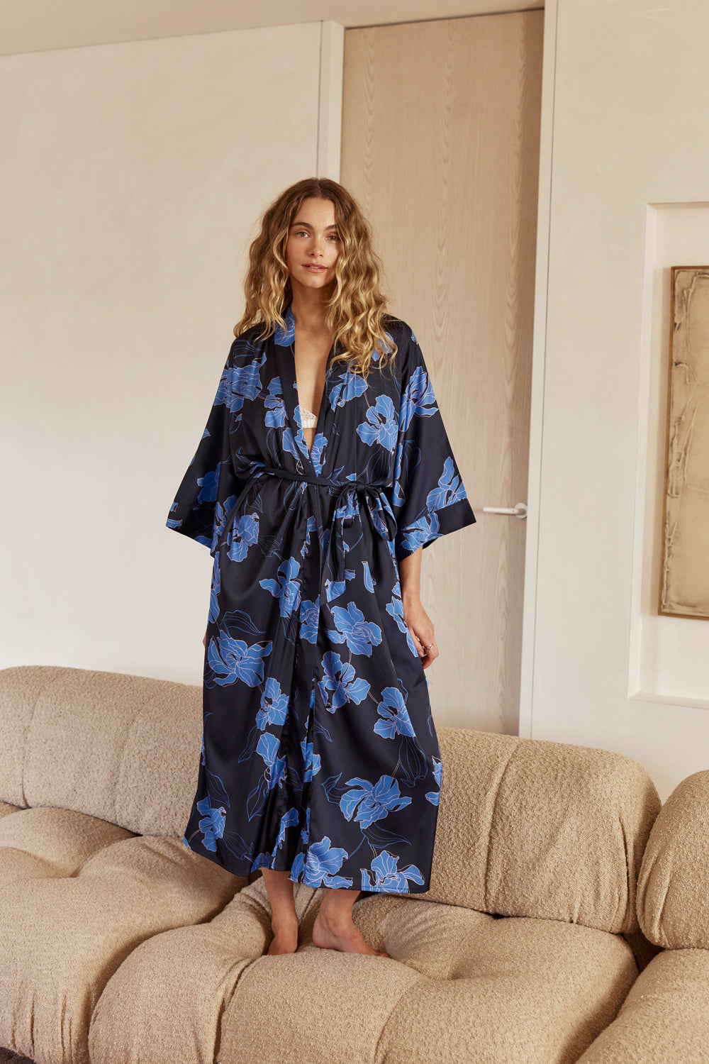 Woman wearing a blue floral robe sitting on a beige couch in a room.