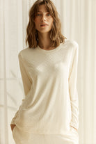 Woman wearing a ellie lightweight velour cable knit set ivory long-sleeve top and pants front on view with curtains in background