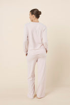 Woman wearing a ellie lightweight velour cable knit set pink long-sleeve top and pants on a beige background back view
