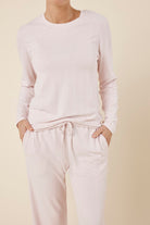Close up shot of woman wearing a ellie lightweight velour cable knit set pink long-sleeve top and pants on a beige background and hands in pockets