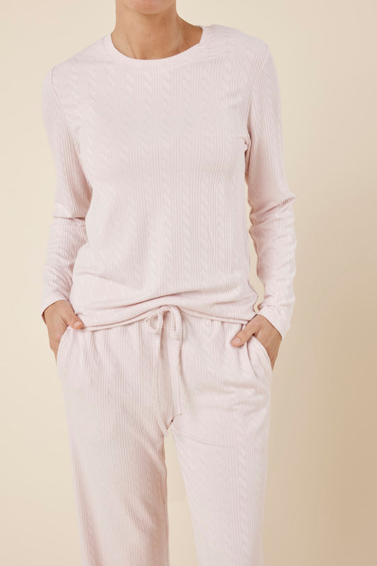 Close up shot of woman wearing a ellie lightweight velour cable knit set pink long-sleeve top and pants on a beige background and hands in pockets