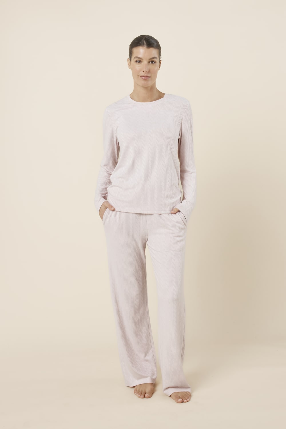 Woman wearing a ellie lightweight velour cable knit set pink long-sleeve top and pants on a beige background front on view