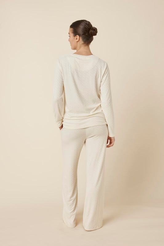Woman wearing a ellie lightweight velour cable knit set ivory long-sleeve top and pants on a beige background back view