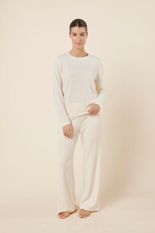 Woman wearing a ellie lightweight velour cable knit set ivory long-sleeve top and pants on a beige background front on view