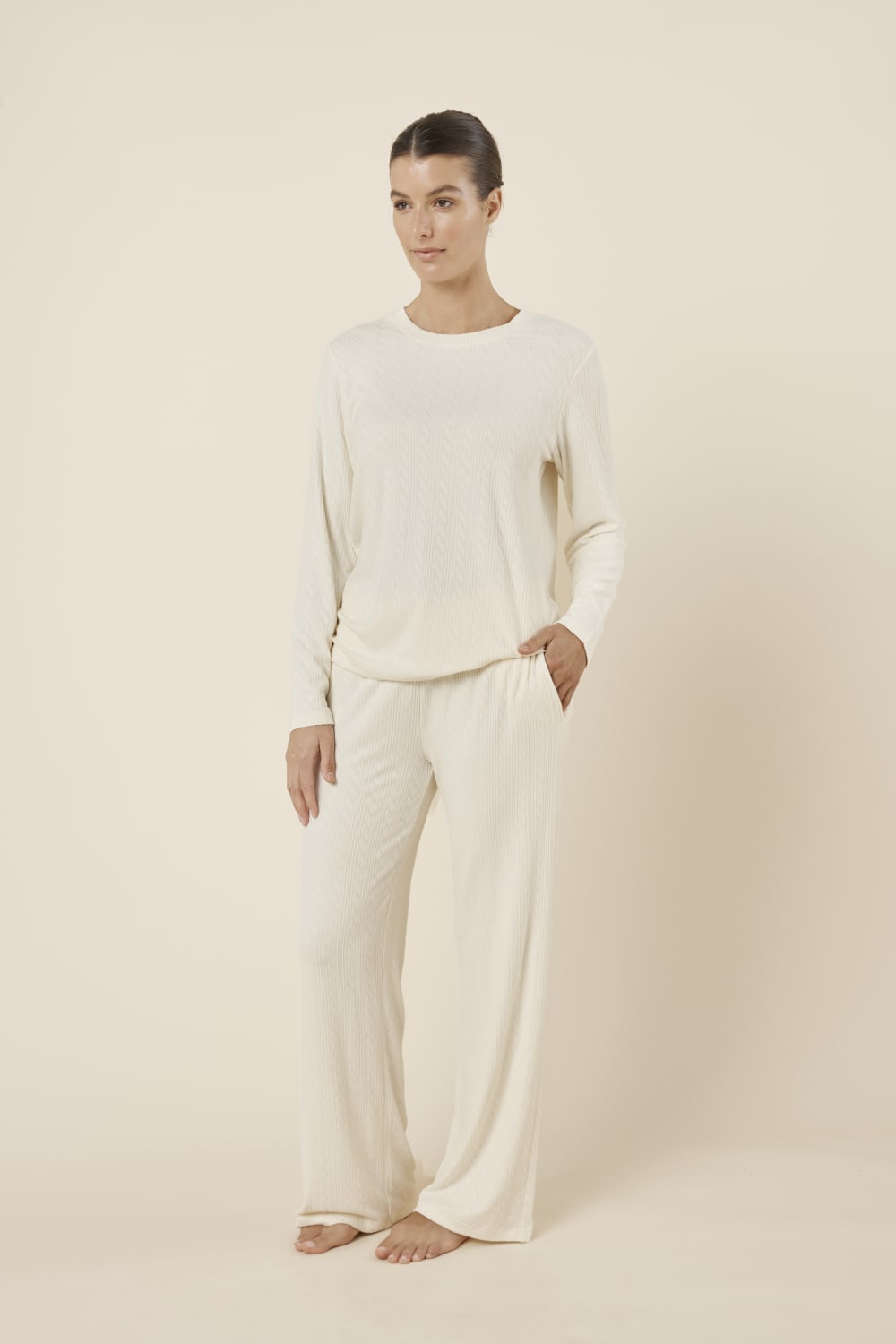 Woman wearing a ellie lightweight velour cable knit set ivory long-sleeve top and pants on a beige background side on view