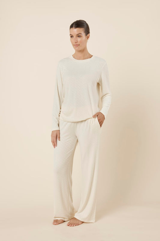 Woman wearing a ellie lightweight velour cable knit set ivory long-sleeve top and pants on a beige background side on view