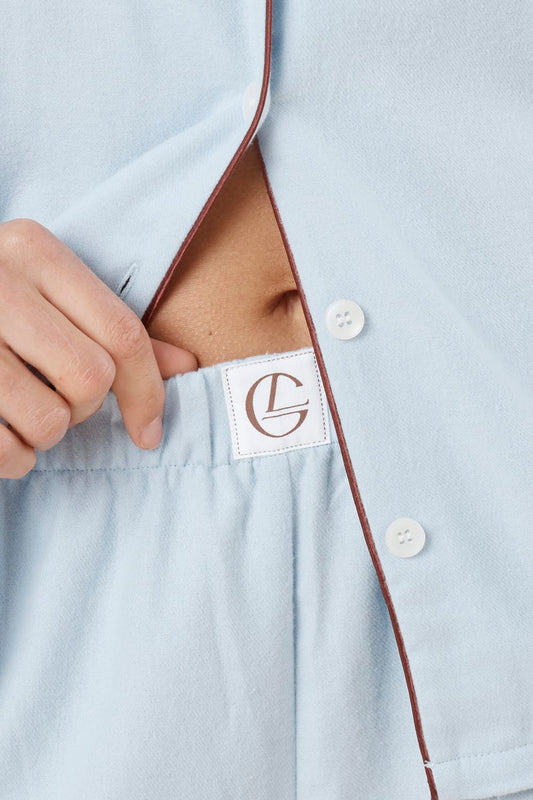 Woman wearing light blue isabella brushed cotton pyjama PJ set with a close up view of small Gingerlilly logo on waistline of pants and shirt hanging over top with white buttons