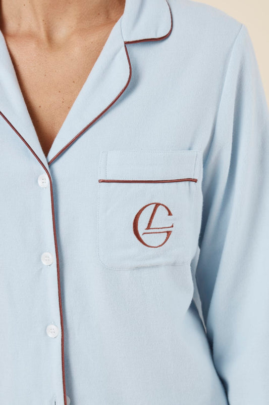 Woman wearing light blue isabella brushed cotton pyjama PJ set with a small red logo on pocket with red pip detailing and white buttons showing