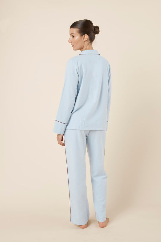Woman wearing light blue isabella brushed cotton pyjama PJ set with a small red logo on a beige background back view with head to side