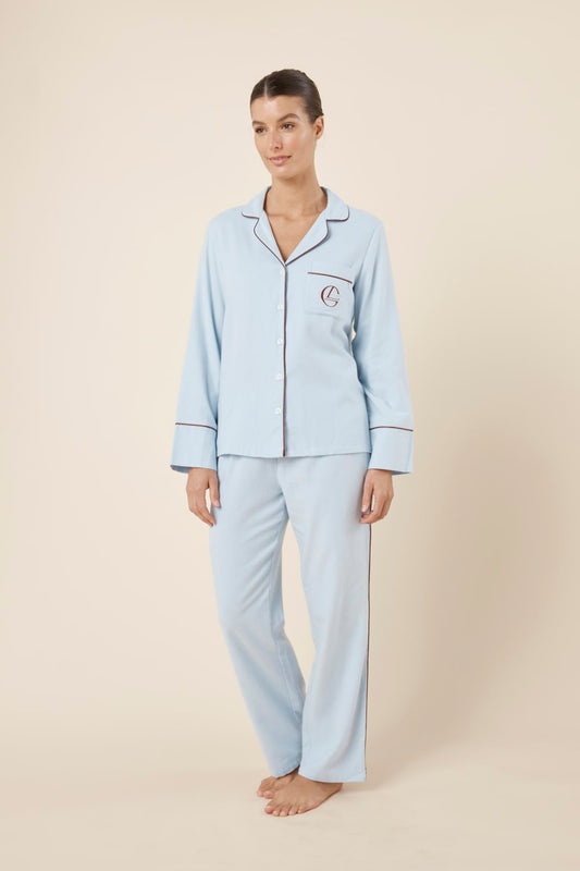 Woman wearing light blue isabella brushed cotton pyjama PJ set with a small red logo on a beige background side on view