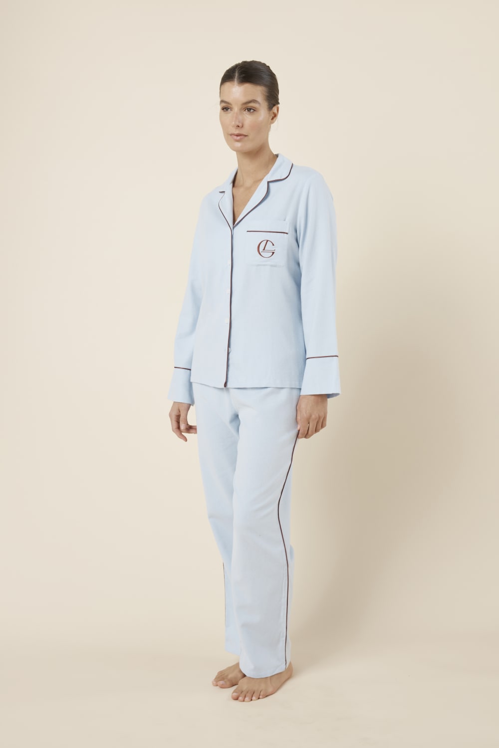 Woman wearing light blue isabella brushed cotton pyjama PJ set with a small red logo on a beige background side on view hands by sides