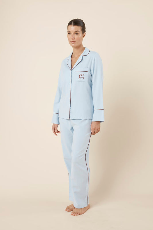 Woman wearing light blue isabella brushed cotton pyjama PJ set with a small red logo on a beige background side on view hands by sides