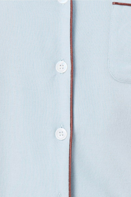 Light blue shirt with white buttons and a brown thread detail on a light gray background