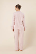 Woman wearing light pink isabella brushed cotton pyjama PJ set with a small red logo on a beige background back view