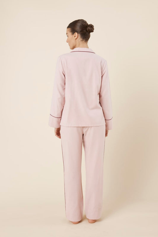 Woman wearing light pink isabella brushed cotton pyjama PJ set with a small red logo on a beige background back view