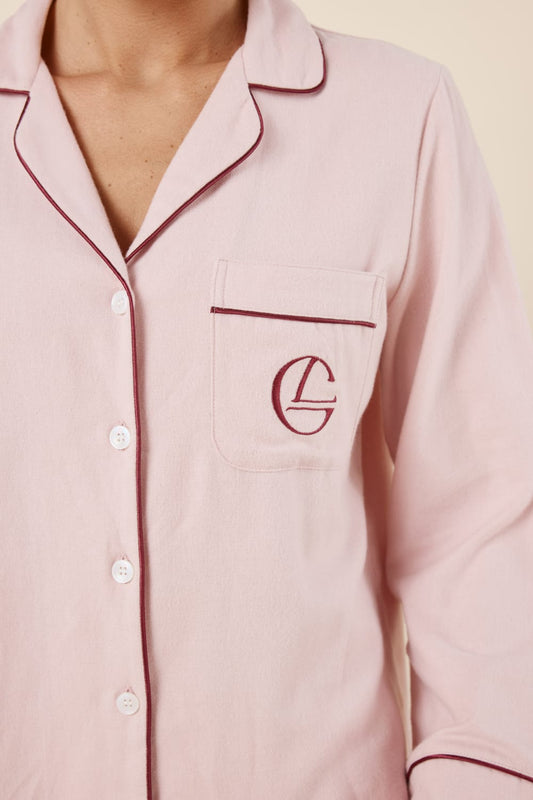 Woman wearing light pink isabella brushed cotton pyjama PJ set top with a small red gingerlilly embroidery logo on pocket with red piping detail and a beige background. 