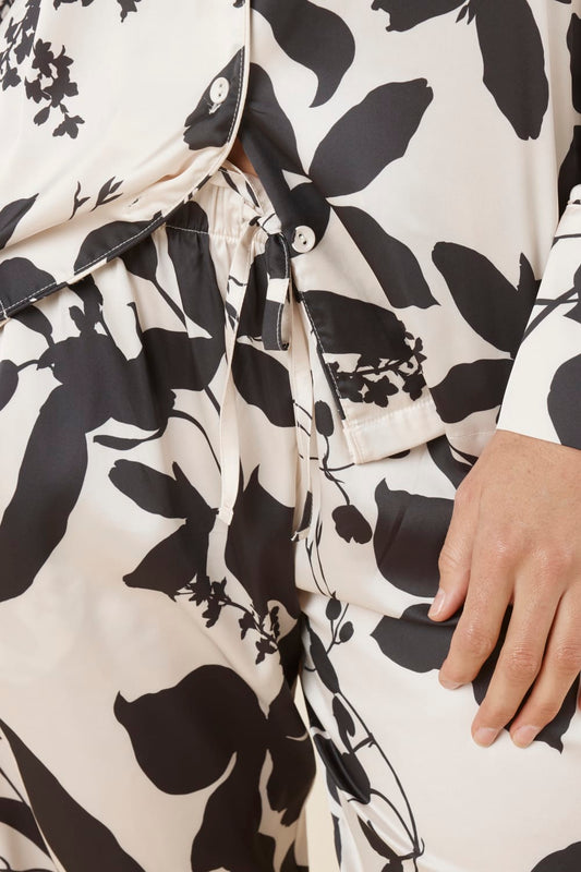 Close-up of a black and white floral patterned Ivy Silky Satin pyjama PJ set with a hand visible and white buttons from the top