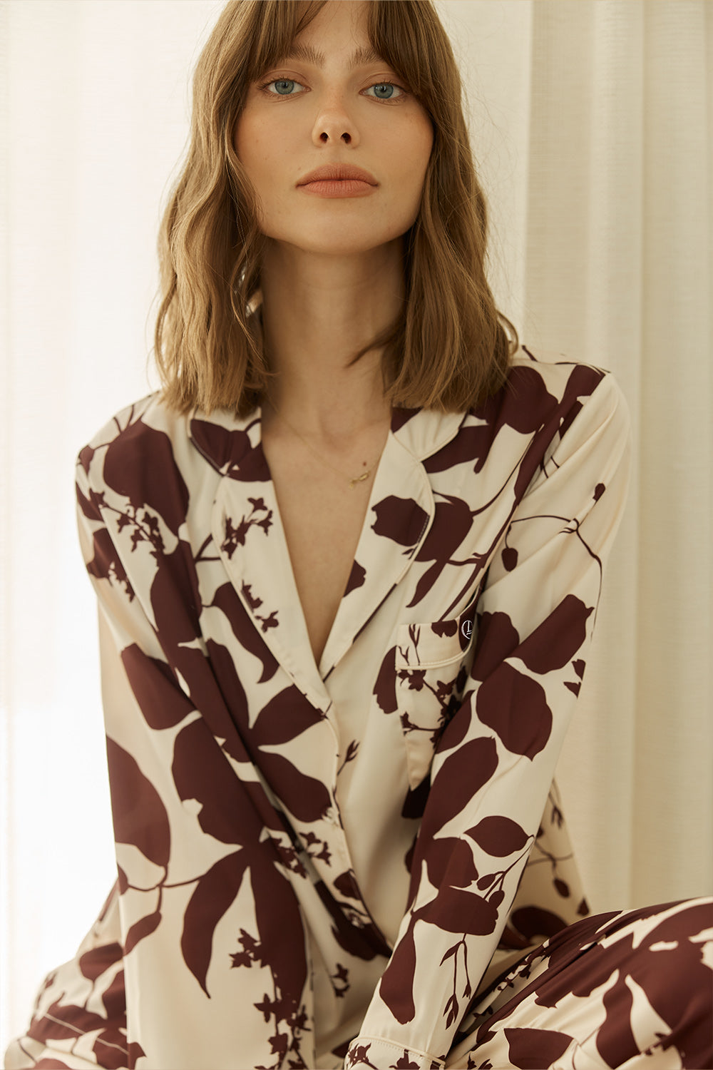 Woman wearing a ivy silky satin pyama PJ set floral pattern while sitting down looing elegant