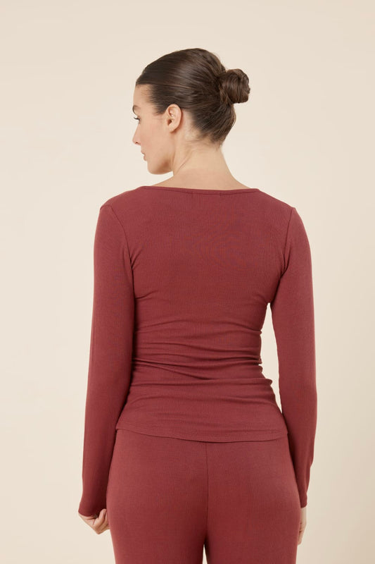 Woman wearing Lille Ribbed Long Sleeve Henley Top Burgundy turned to show the back view, highlighting the smooth ribbed texture and fitted shape.