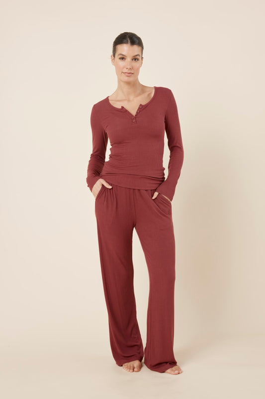 Woman wearing Lille Ribbed Long Sleeve Henley Top Burgundy standing in matching burgundy bottoms, showing the coordinated lounge set and fitted ribbed fabric.