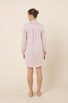 Woman wearing a pink striped Lolita Stripe Night Shirt dress against a beige background back view with arms beside her