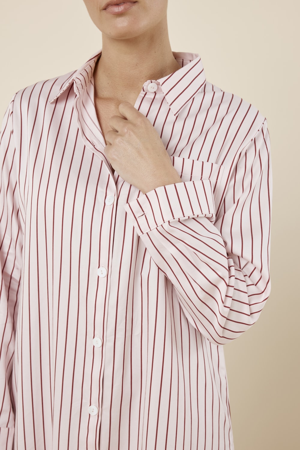 Woman wearing a pink striped Lolita Stripe Night Shirt dress against a beige background front on close view with arm near neck