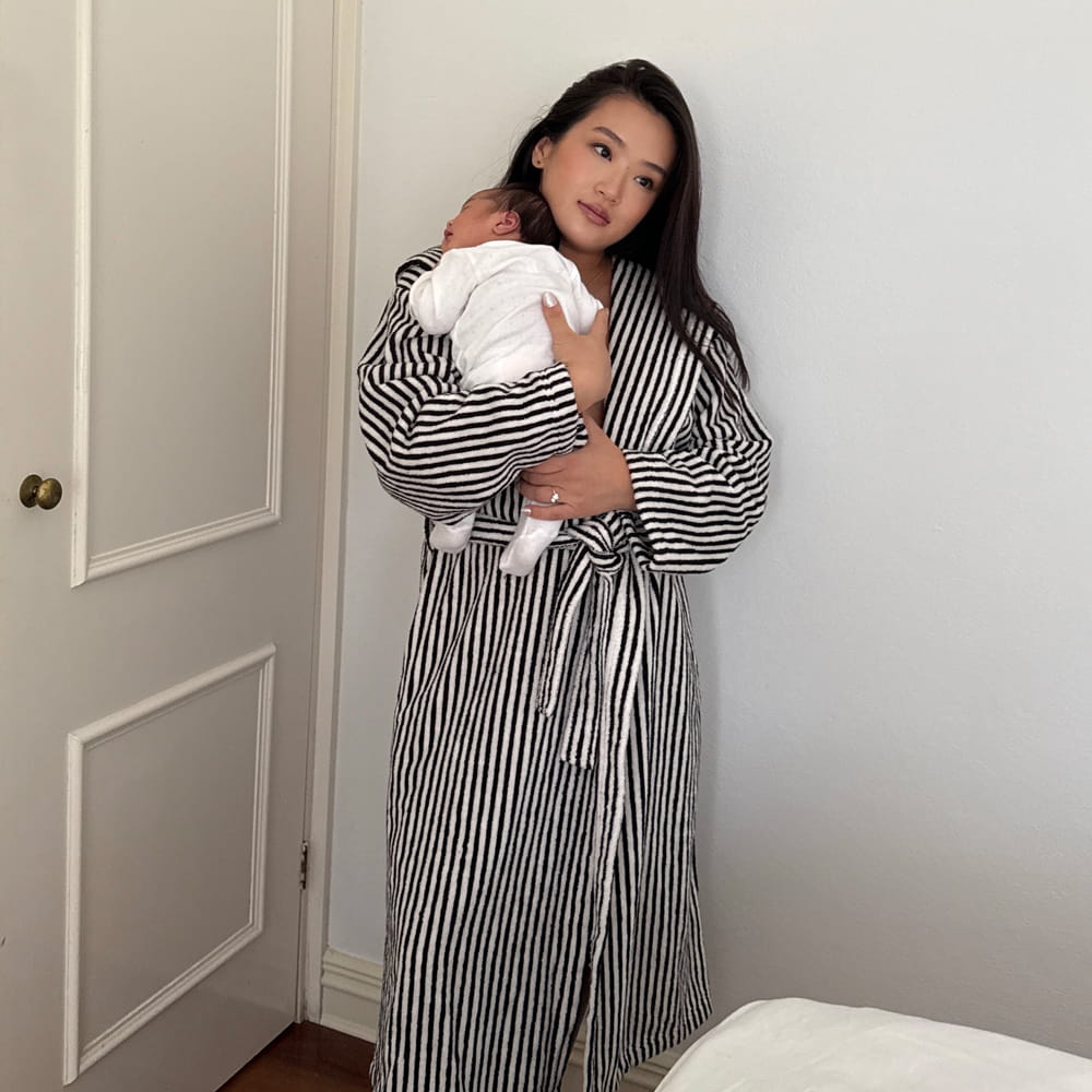 Woman in a striped robe holding a baby in a room with a white door.
