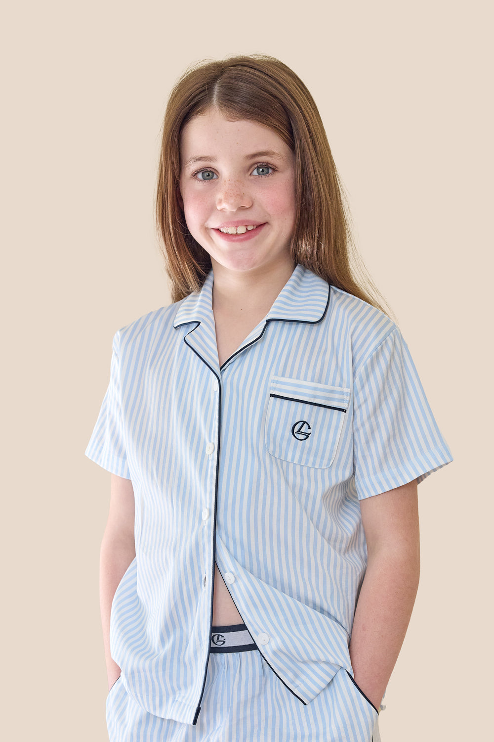 Young girl wearing a light blue striped pajama set on a beige background