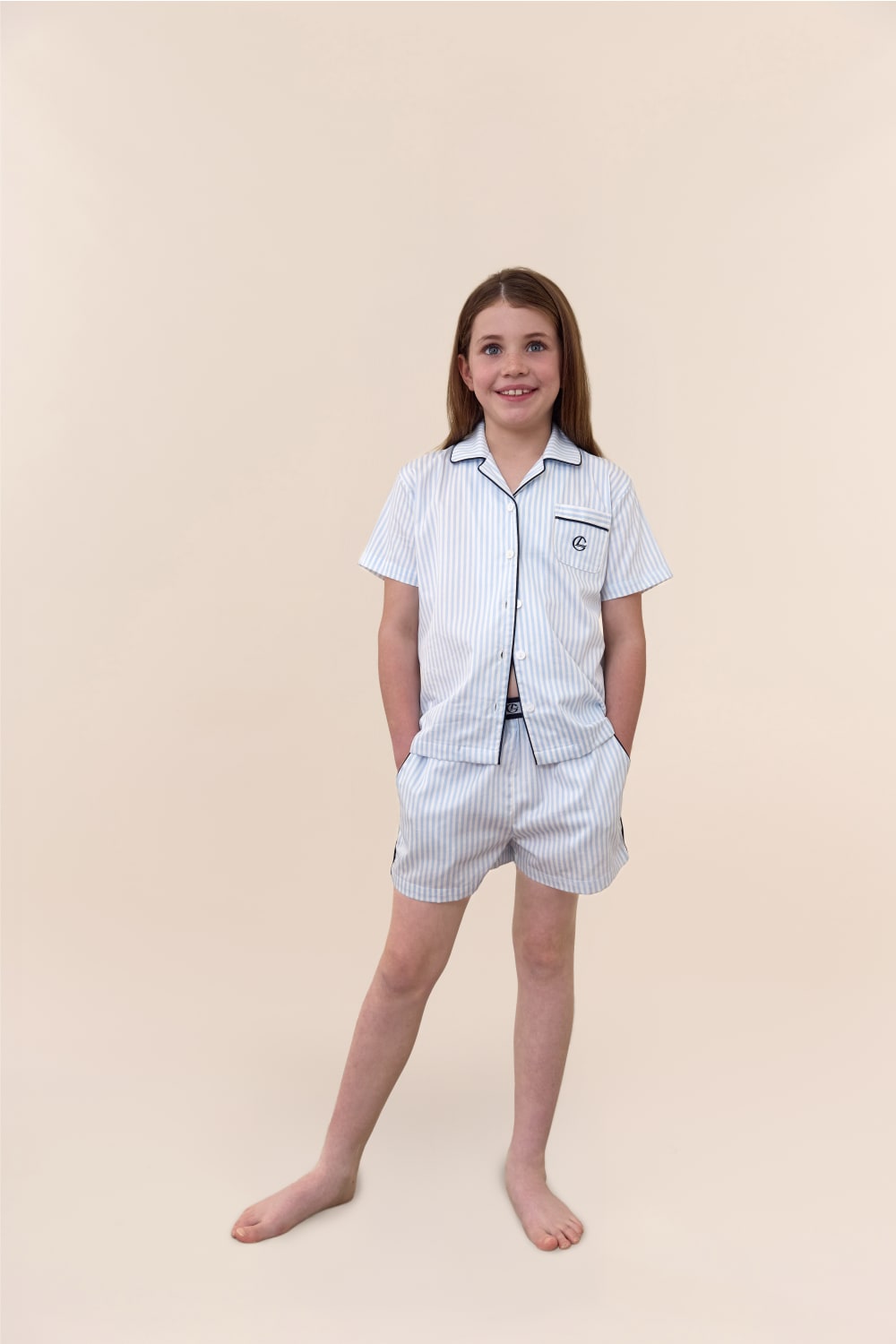 Young girl wearing a white pajama set with black trim on a beige background