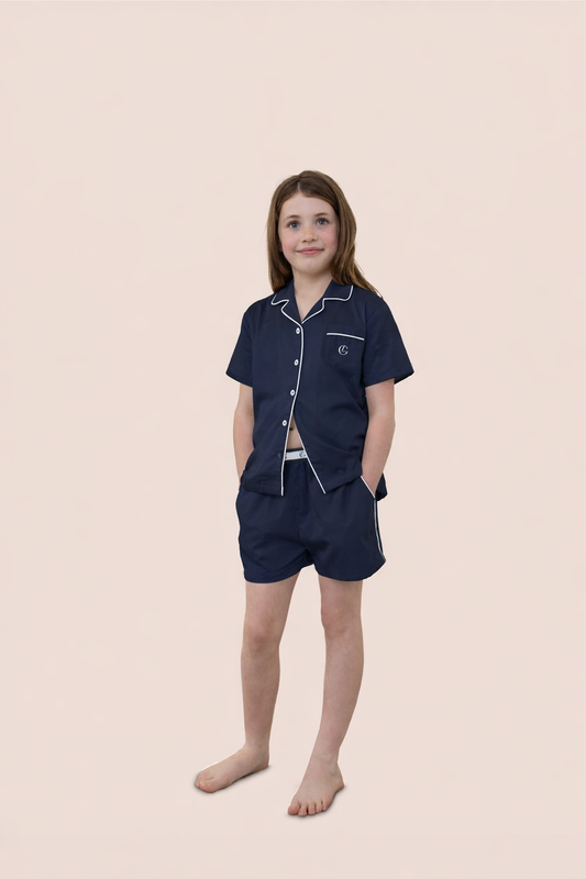 Young girl wearing a navy pajama set with white piping on a beige background