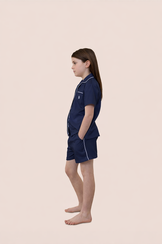 Girl wearing navy pajama set with white piping on a beige background