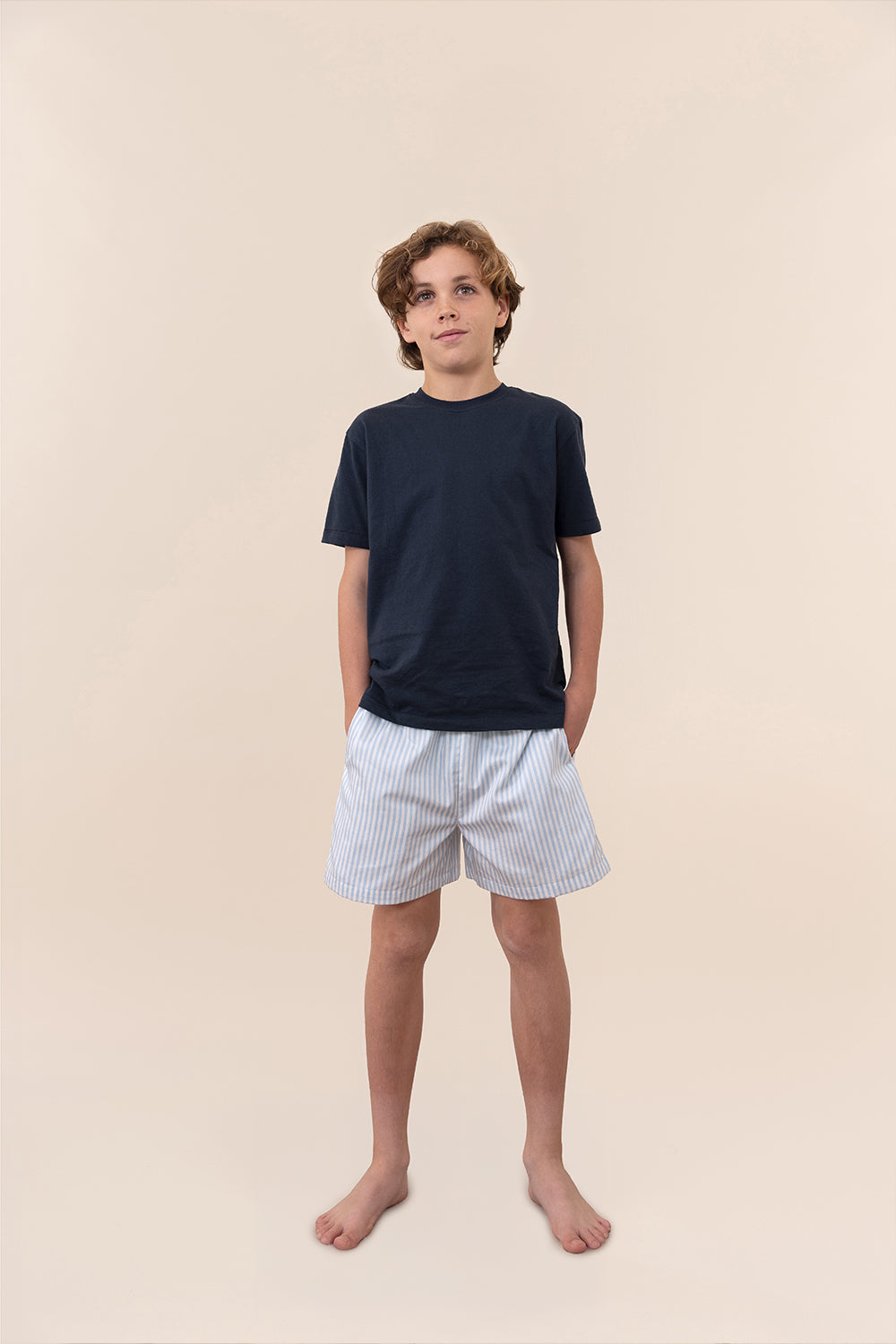 Young boy wearing a navy t-shirt and light-colored shorts on a beige background