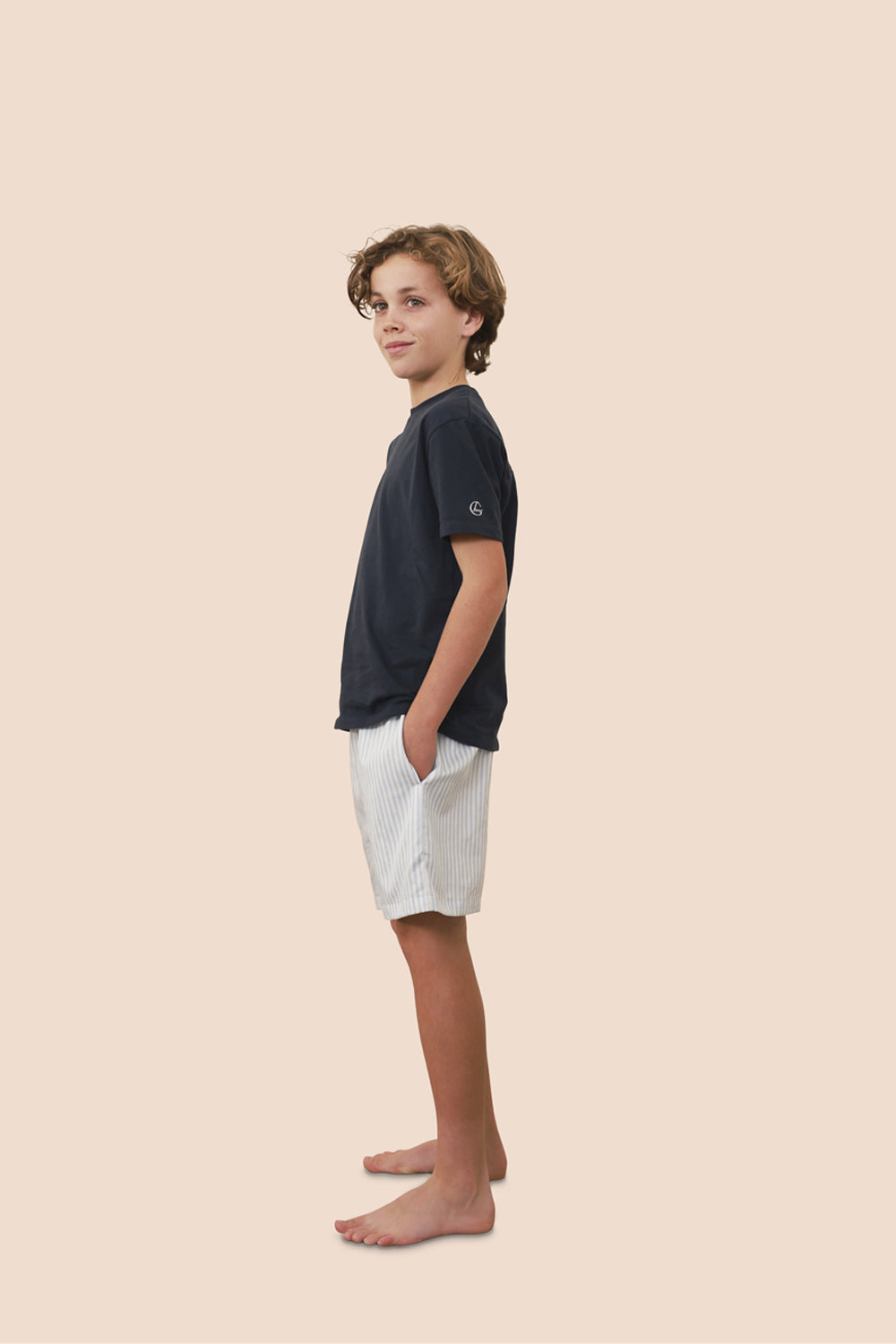 Young boy wearing a black t-shirt and white shorts on a beige background