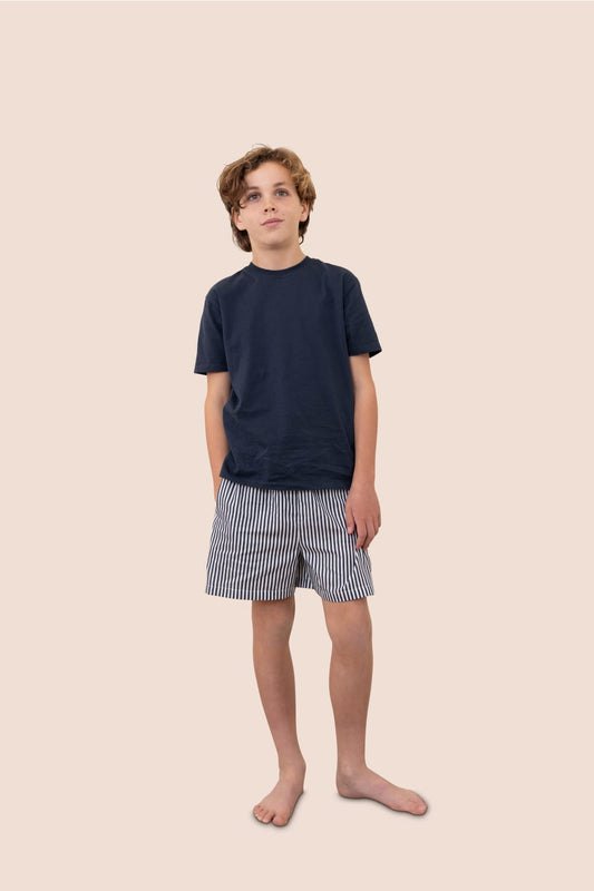 Young boy wearing a navy t-shirt and striped shorts on a beige background